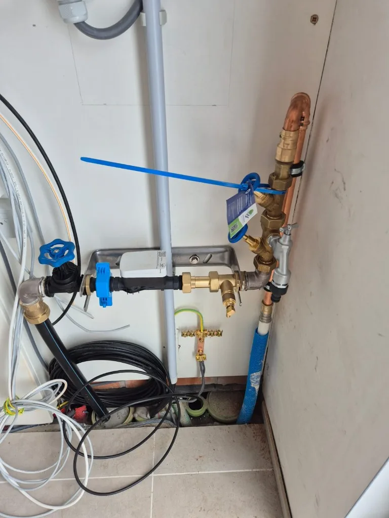 Watermeter met afsluitkraan en aarding in een technische ruimte, klaar voor waterkeuring